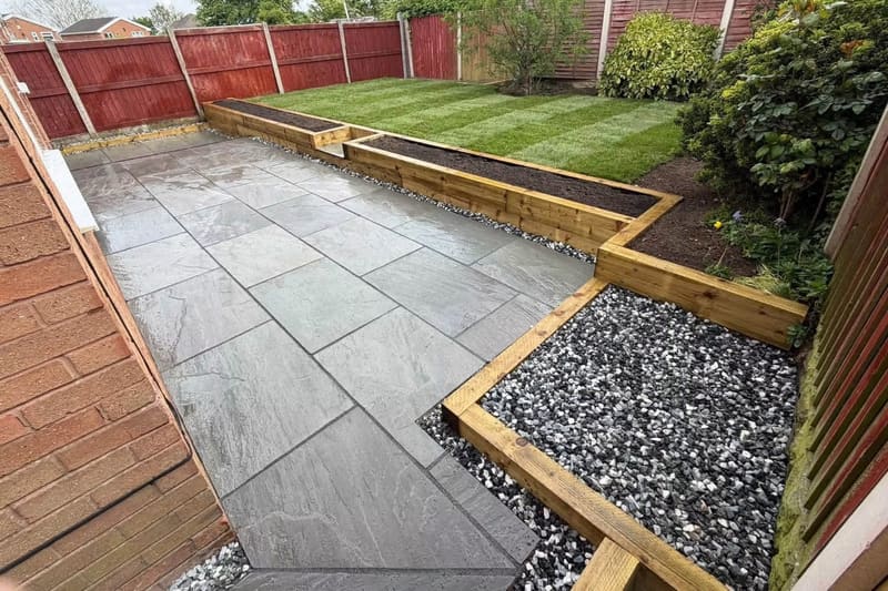 A finished patio in grey riven porcelain running up to a timber sleeper retaining edge and new turf.