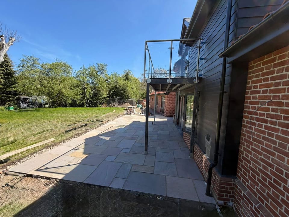 Riven sandstone paving laid across the terrace under a glass balcony.