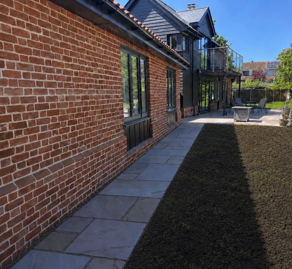 The finished paved path along the brick wall of the house, with new turf beside it.