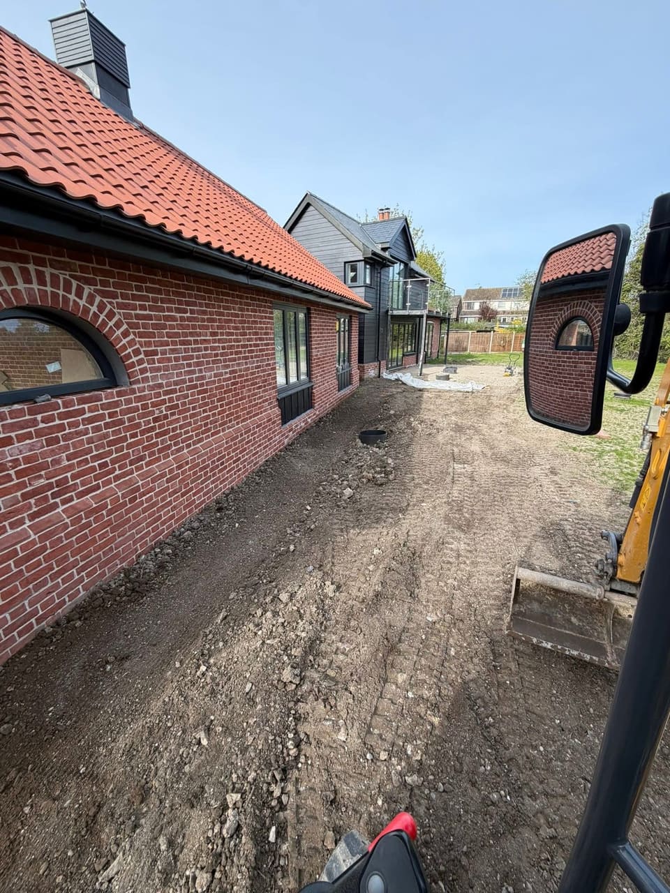 Excavated ground alongside a house, photographed from the cab of a tracked excavator.