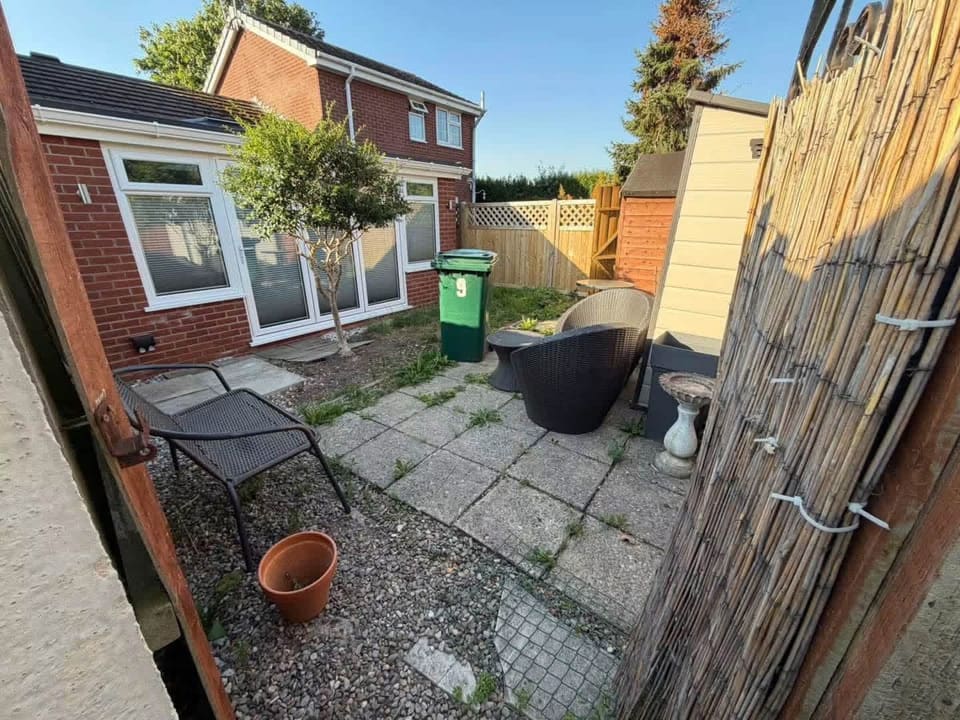 An old patio before it came out: small slabs, weeds in the joints, a garden table and chairs.