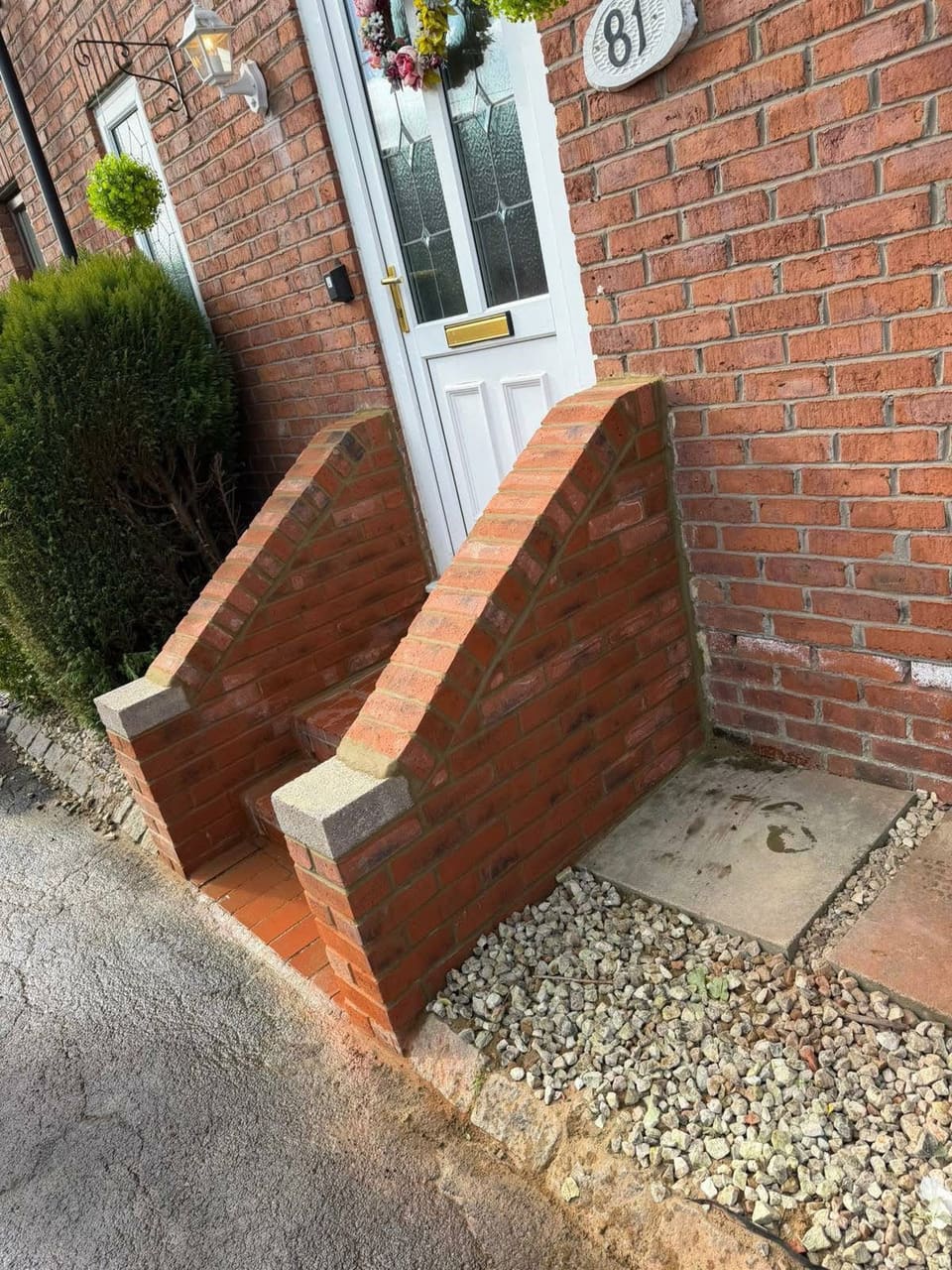 A finished brick cheek wall and step at a front door with the house number above.