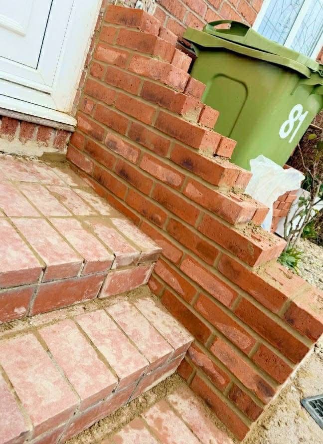 Brick steps with a galvanised handrail at a front door, a green bin beside them.