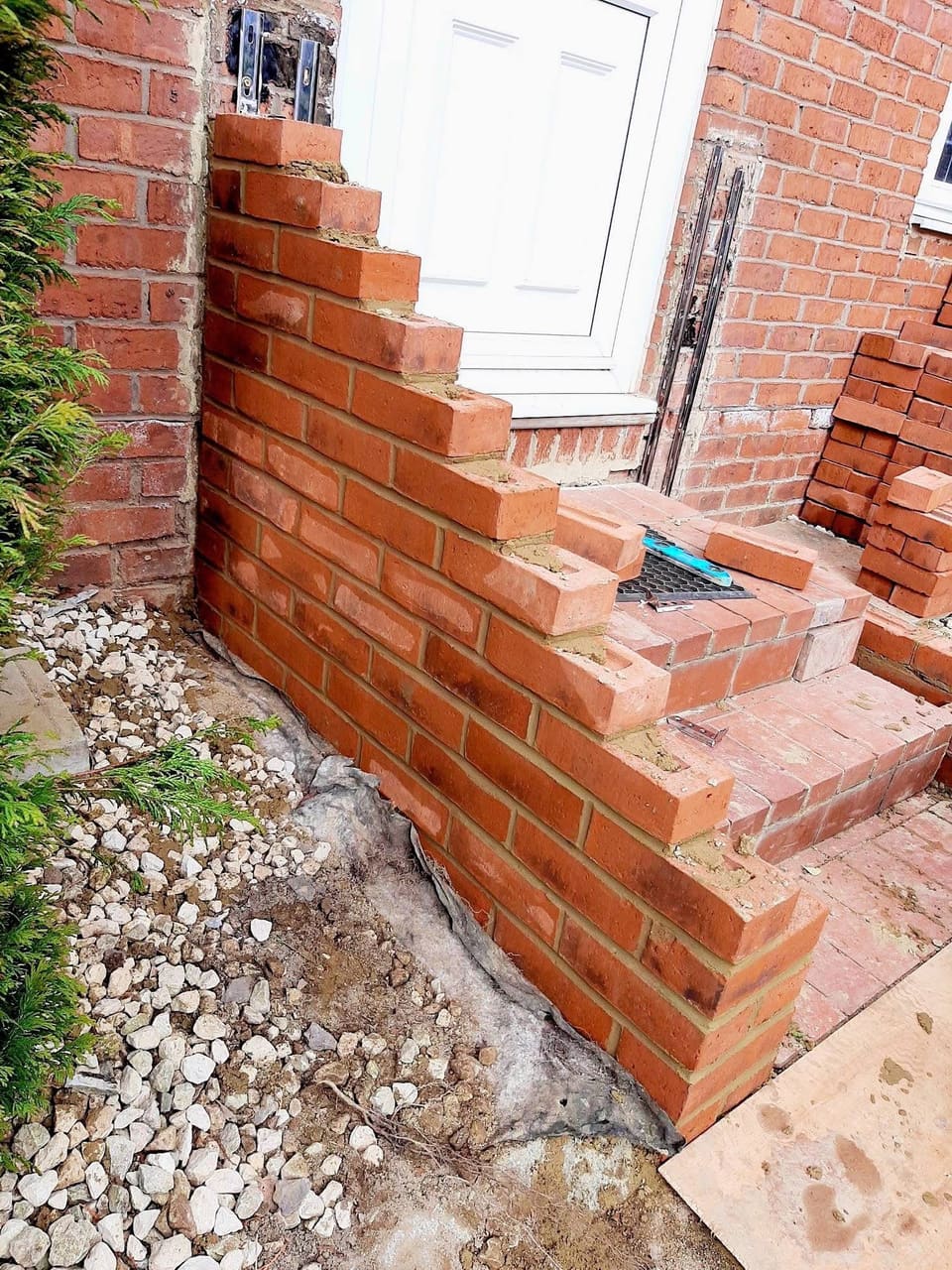 Brick steps under construction at a front door, with bricks stacked on the path.