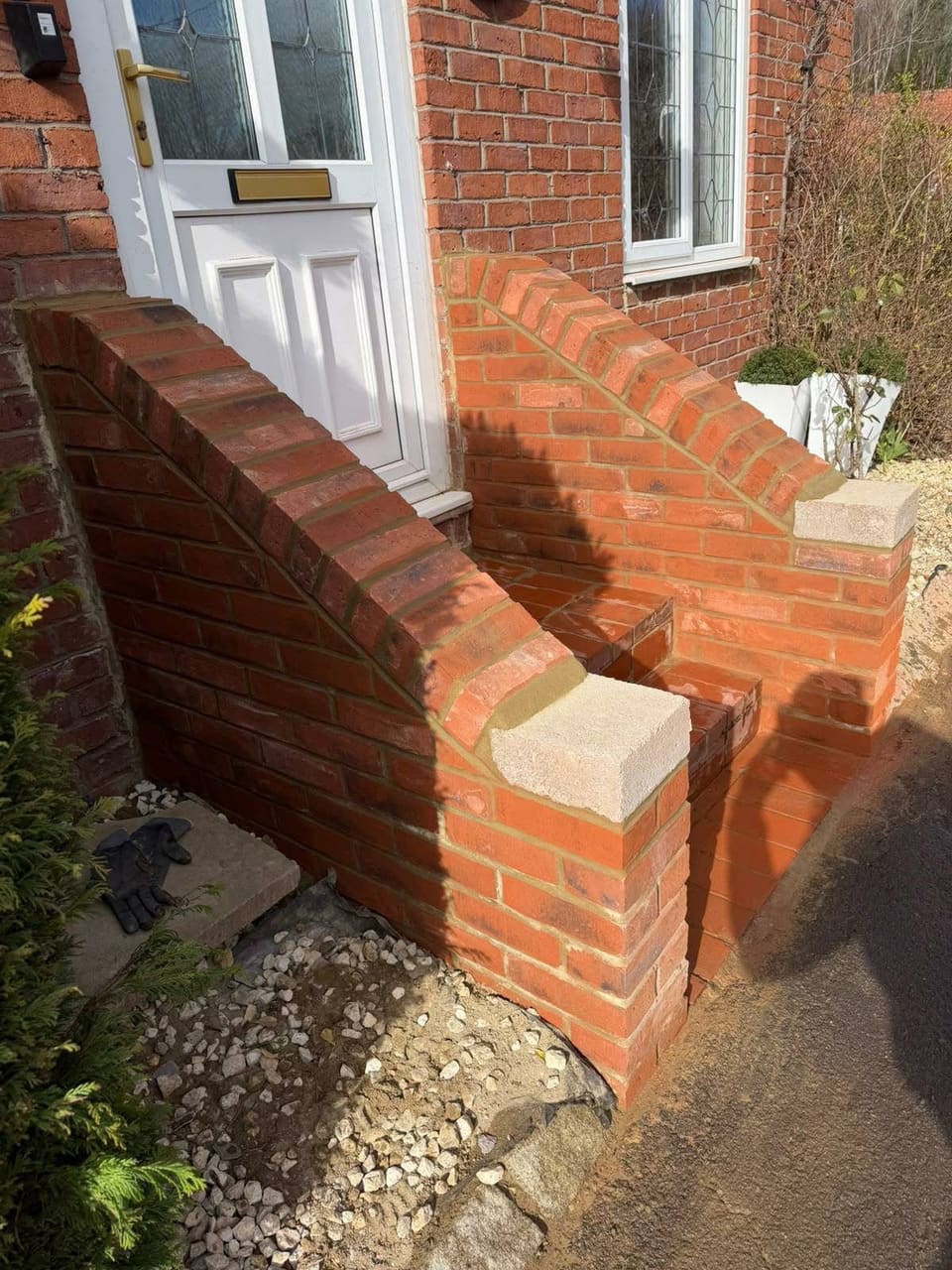 A raked brick cheek wall being built beside a front door, with the ground beneath it open.