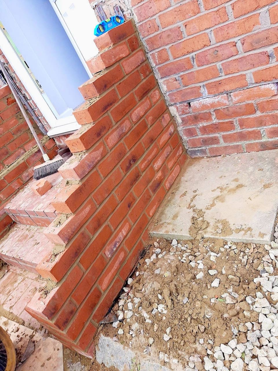 The side of a brick doorstep under construction, the cheek wall part built and the ground beneath opened up.