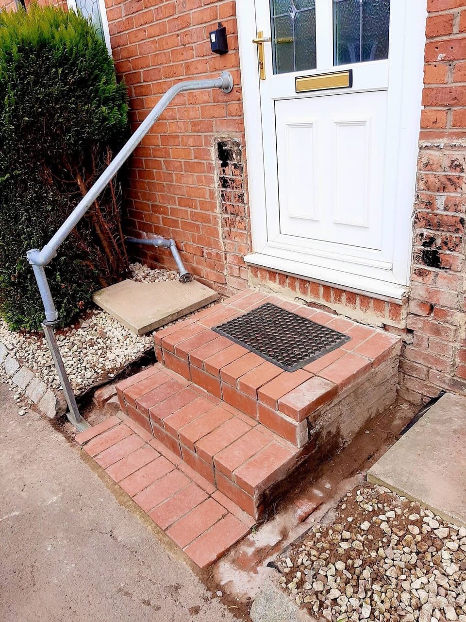Brick steps up to a front door with a galvanised handrail and a coir doormat.