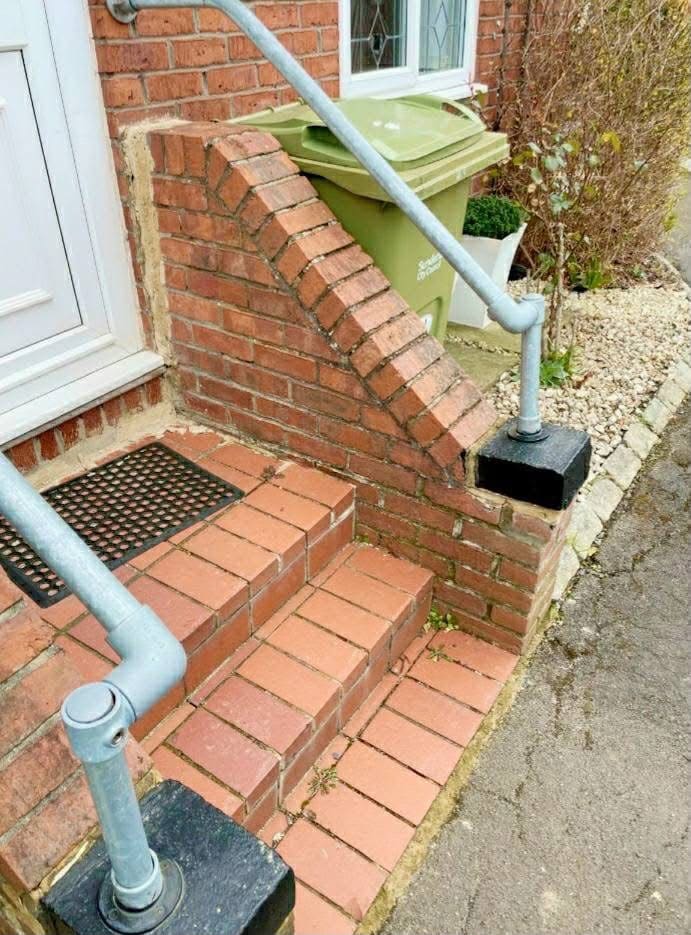 Finished brick steps and a raked brick cheek wall at a front door, with a galvanised handrail either side.