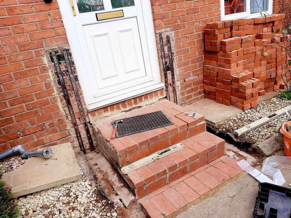 The same doorstep with the ground open, bricks stacked and the handrail fittings on the floor.