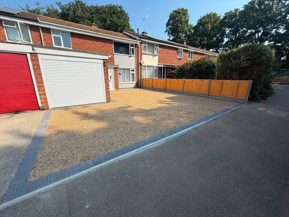 A finished gravel driveway with charcoal block paved edging, running up to a red and a white garage door.