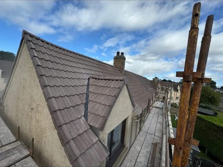 A gable and dormer re-covered in new concrete interlocking tile under a blue sky.
