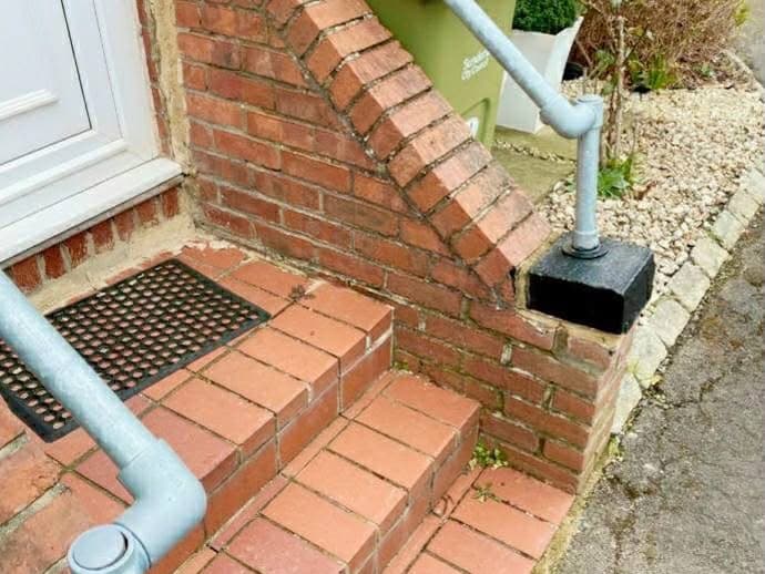 Finished brick steps and a raked brick cheek wall at a front door, with a galvanised handrail either side.