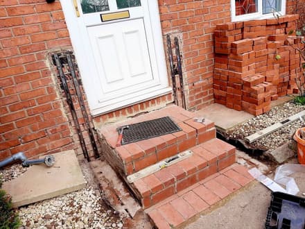 The same doorstep with the ground open, bricks stacked ready and the handrail fittings on the floor.
