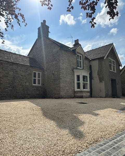 A gravel driveway laid across the front of a stone house with a bay window, under a blue sky.