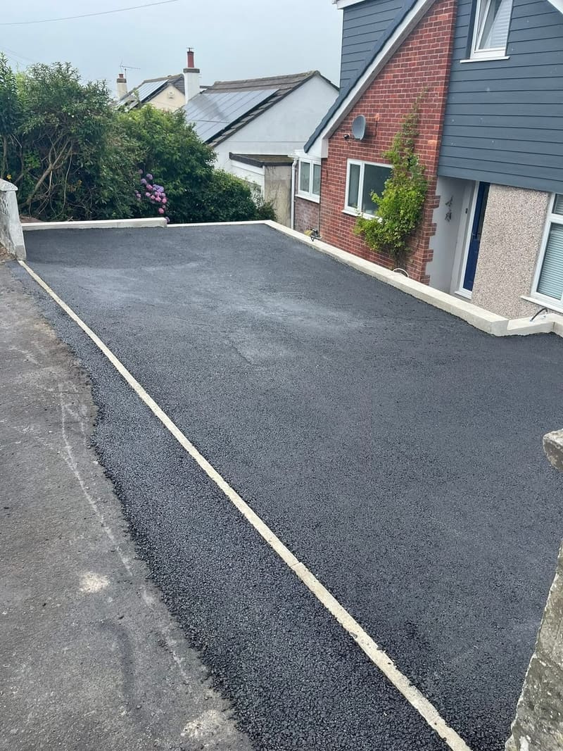 A finished black tarmac driveway running up to a house, with a white rendered retaining wall along one side and a painted white edge line.