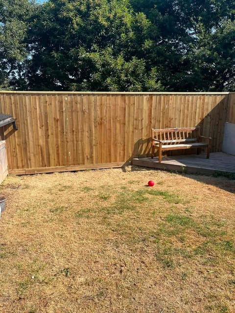 A new close board timber fence along the end of a garden, with a wooden bench on a decked corner beside it.