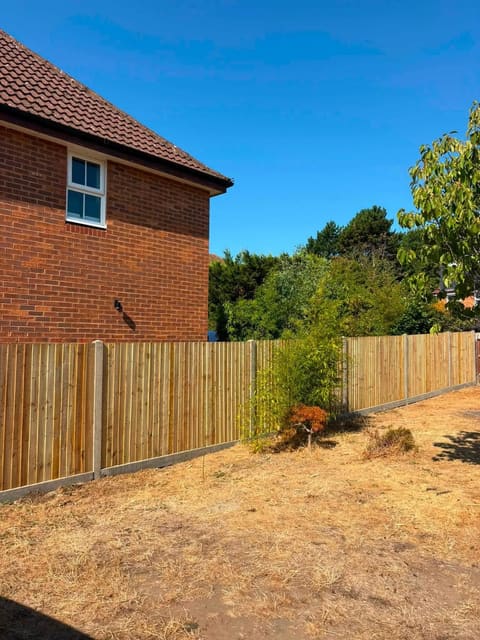 A new close board timber fence on concrete posts with concrete gravel boards, running along a boundary with bare ground in front of it.