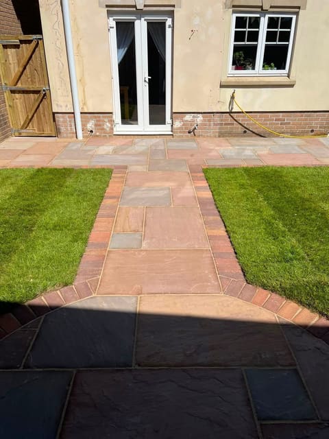A riven sandstone path with a red brick soldier edge running up to white french doors, with a strip of turf either side.