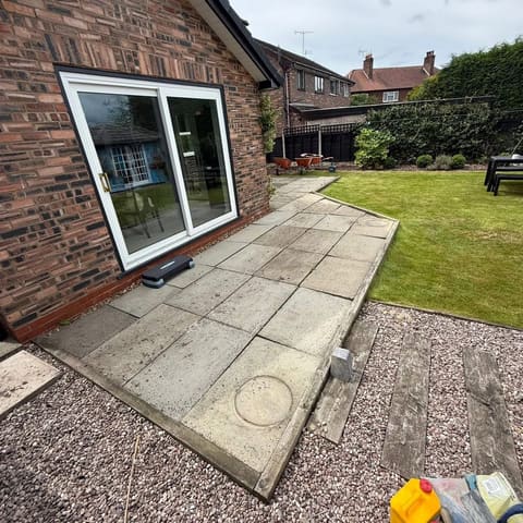The same doors before the work, with old concrete slabs, a manhole ring and loose gravel.