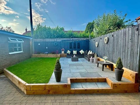 The same garden from the other end: grey paving, a lawn held by a timber sleeper edge, and clipped shrubs in pots against a dark grey fence.