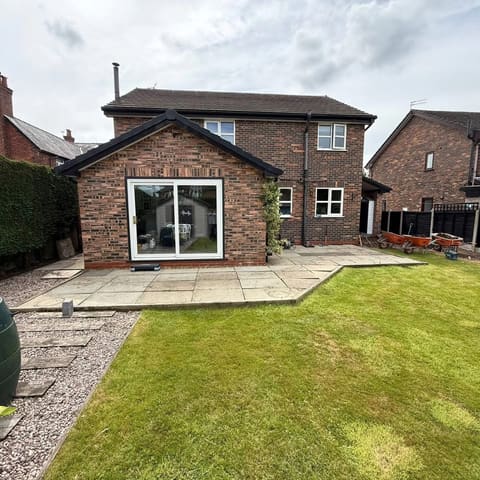 The same house from the same spot before the work, with an old light concrete slab patio and wheelbarrows on the grass.