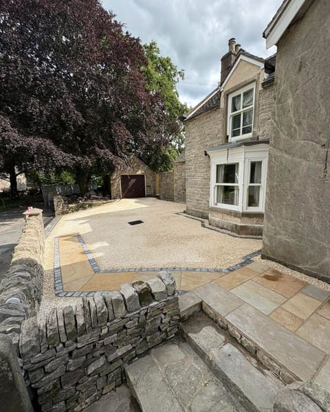 A stone house with new riven sandstone paving, a gravel area and stone steps, beside a dry stone wall.