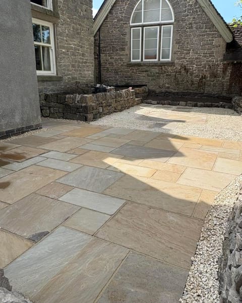 New sandstone paving running along a stone house to a low stone retaining wall, with an arched window above.