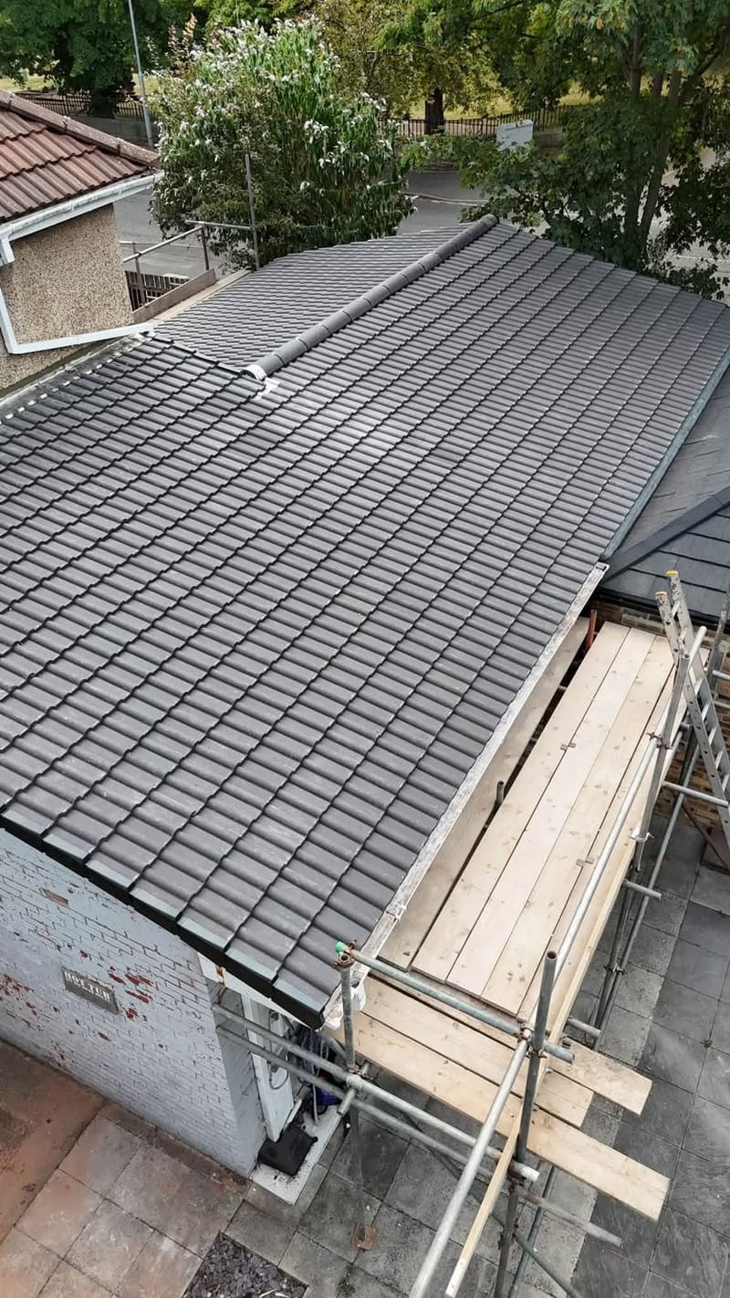 The same roof from the scaffold end, newly covered in grey interlocking tile with the eaves finished in black.