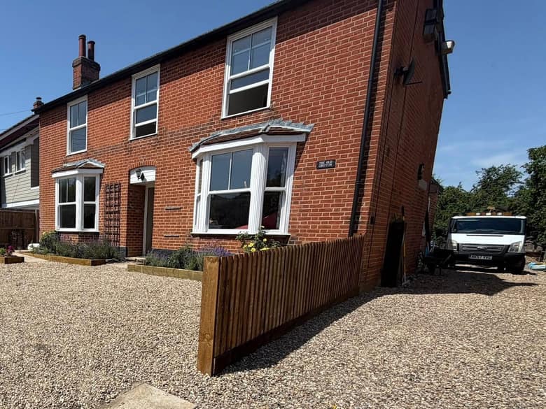 A new close board timber fence beside a gravel driveway at the front of a red brick house.