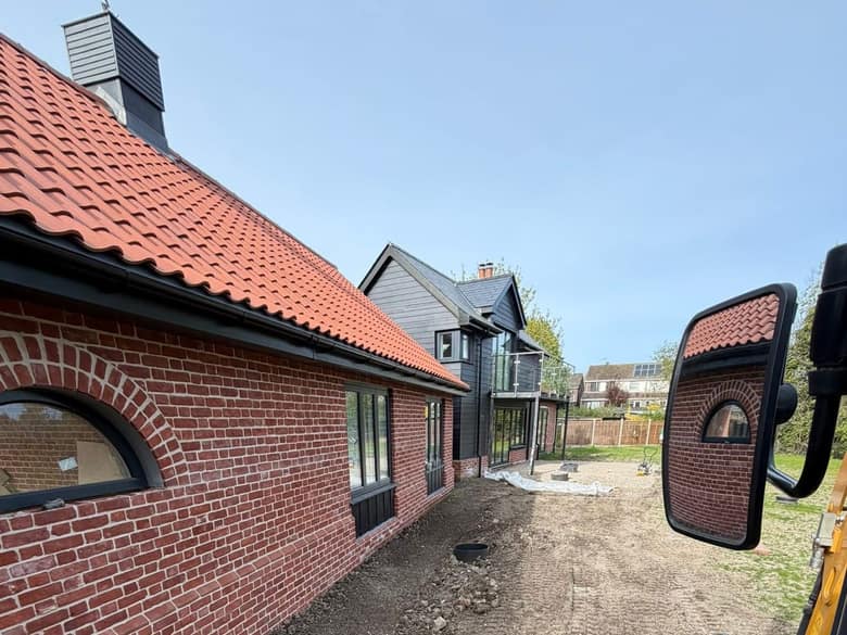 Excavated ground alongside a house, photographed from the cab of a tracked excavator.