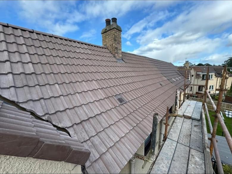 A finished roof in new concrete interlocking tile, running up to a stone chimney, photographed from the scaffold.