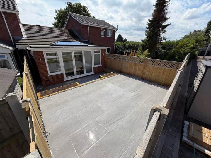 A large finished porcelain patio behind a house extension, with a timber fence around it.