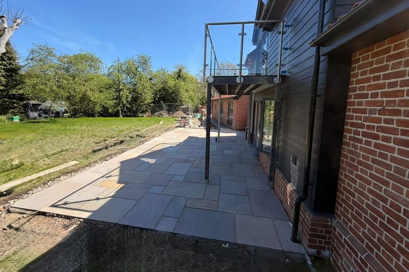 Riven sandstone paving laid across the terrace under a glass balcony.