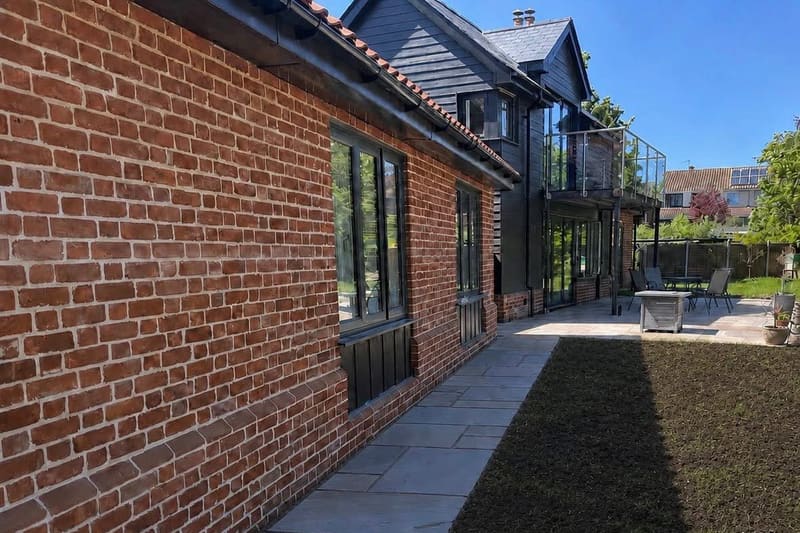 The finished paved path running along the brick wall of the house, with new turf laid beside it.