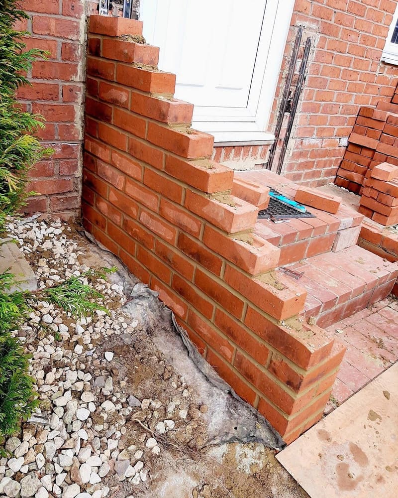 Brick steps under construction at a front door, with bricks stacked on the path ready to lay.