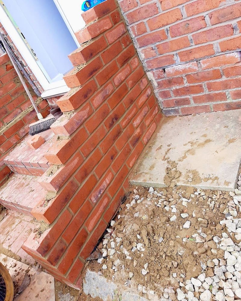 The side of a brick doorstep under construction, the cheek wall part built and the ground beneath it opened up.