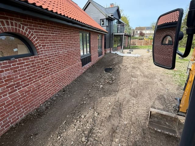 Excavated ground alongside a house, photographed from the cab of a tracked excavator.