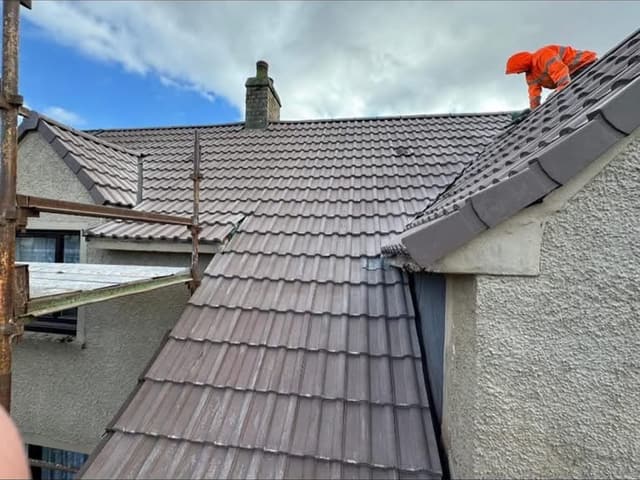 A roofer in orange hi vis working along the ridge of a newly tiled roof.